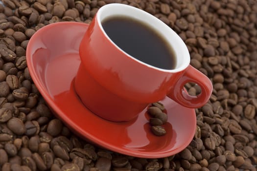 diagonal view of red coffee cup with plate full of coffee beans on white background