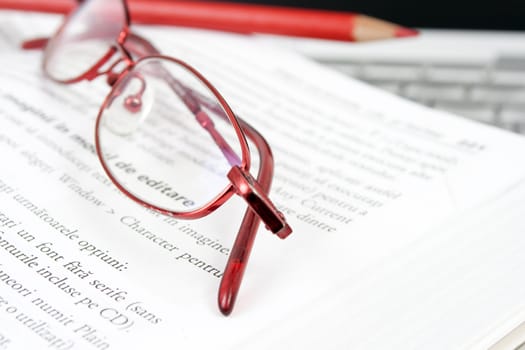 open book on a leptop with a pair of red glases and a red pencil