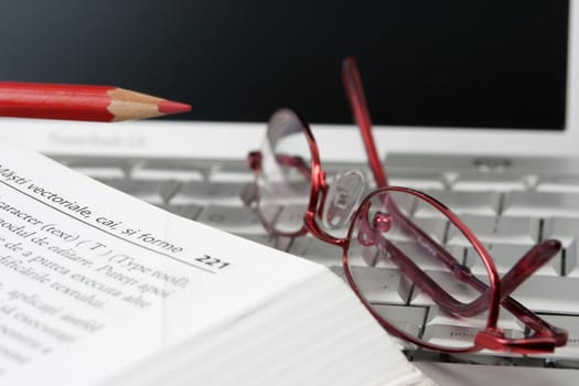 open book on a leptop with a pair of red glases and a red pencil