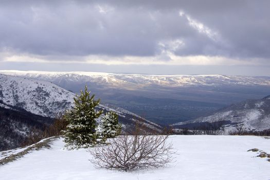 Winter landscape in the mountains. Morning on a cloudy day, the sun's rays peep through the clouds and fall on the snow-capped peaks, below you can see the valley and the city. Yalta, Crimea