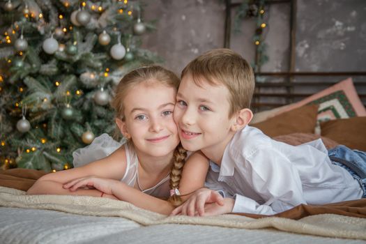 Cheek-to-cheek sister and brother lying on sofa under Christmas tree