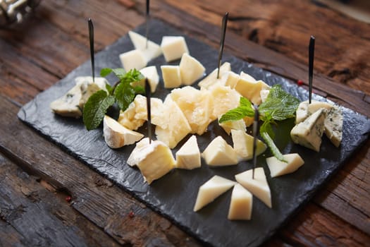 Cheeseboard with Sliced Limburger, Herve Cheese or Reblochon And Blue Gorgonzola, Roquefort or Stilton. Cheese Course with Mix of Yellow and Blue Cheeses Top View on Black Stone Plate Background