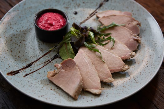 Sliced cold baked pork with herbs on blue plate.