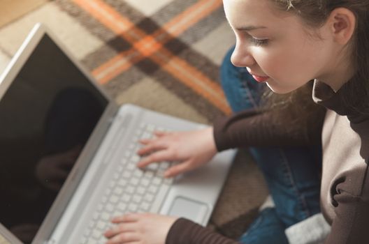 Top view of young teen girl couch prepares report on business lesson, corrects mistakes, keyboards on laptop computer, searches information. Student does homework task