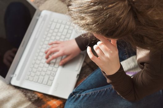 Top view of young teen girl couch prepares report on business lesson, corrects mistakes, keyboards on laptop computer, searches information. Student does homework task