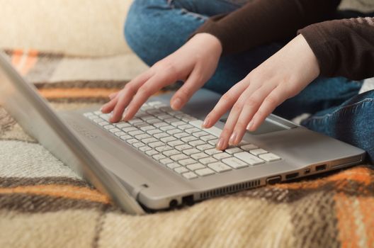 Close up cropped photo of nice hands of woman typing on the laptop at the top of couch
