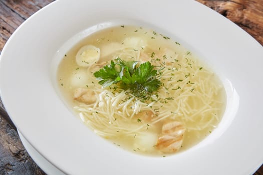 Chicken soup with noodles and vegetables in white bowl.