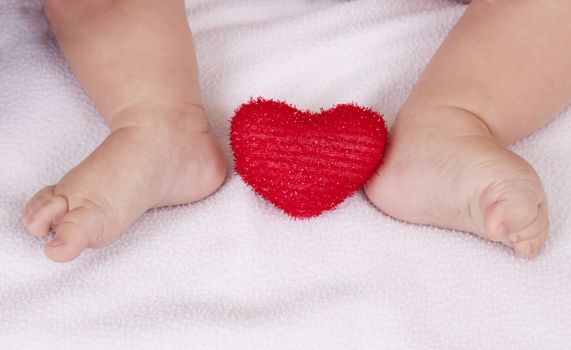 small baby feet with red heart between on white background