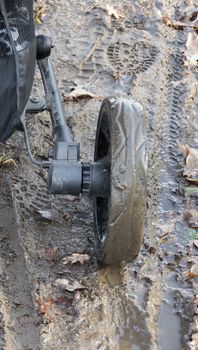 Dirty, mud baby stroller wheels in the muddy ground close up photo.