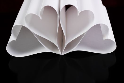white paper hearts in a flower shape on black table with reflection