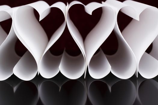 white paper hearts in a raw with reflection on black surface
