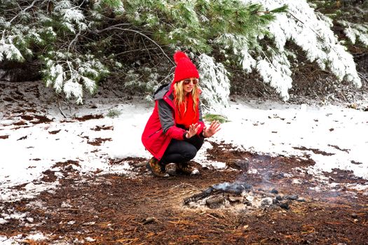 Crouching down by the fire warming stinging frost bitten hands in snowy pine landscape