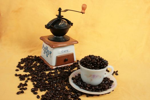 coffee cup full of cofee and a coffee grinder on yellow background