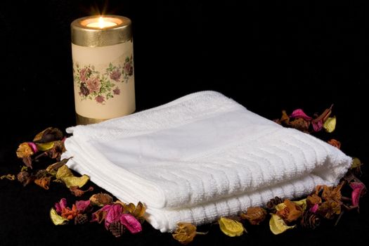 towel candle and dried flowers on black background