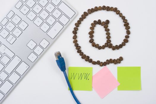 e-mail symbol @ made from coffee beans with computer keyboard and sticky notesand a blue network cable