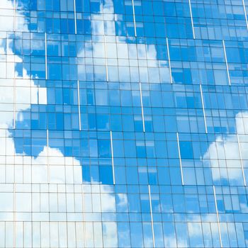 Blue sky and white clouds reflection on glass facade of a modern office building