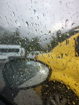 The road with the cars is photographed through the rain splattered windshield of the car.