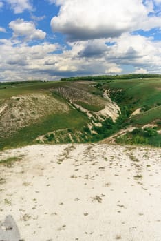 Beautiful view of grassy ravine on sky background with clouds, vertical shot.