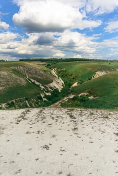 Beautiful view of grassy ravine on sky background with clouds, vertical shot.