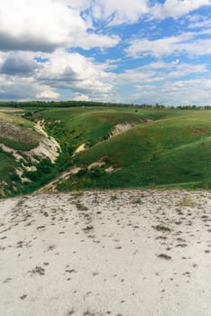 Beautiful view of grassy ravine on sky background with clouds, vertical shot.