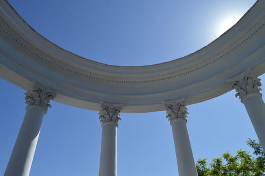 Part of a white rotunda with columns against a blue sky on a Sunny day.