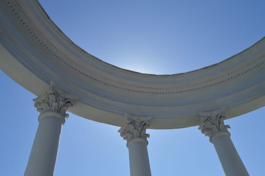 Part of a white rotunda with columns against a blue sky on a Sunny day.