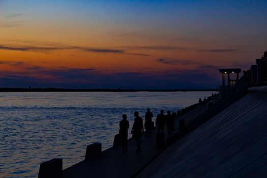 Sunset on the embankment of the Amur river in Khabarovsk. The sun set over the horizon. The embankment is lit by lanterns. People walk along the river Bank.