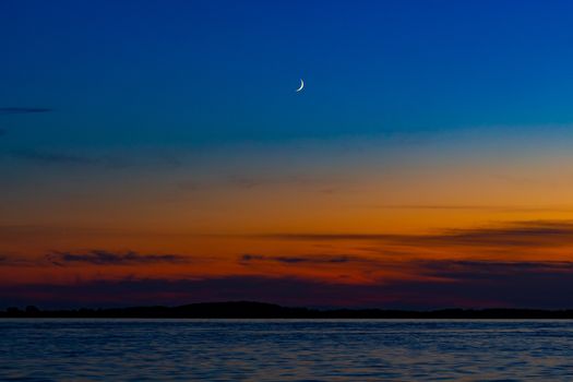 Sunset on the embankment of the Amur river in Khabarovsk. The sun set over the horizon. The embankment is lit by lanterns. People walk along the river Bank.