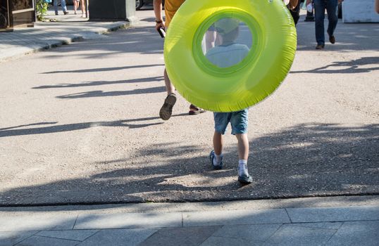 A boy pulls a large green buoy from behind.