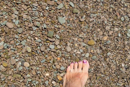 Tanned leg of a woman on a pebble beach against the sea and waves.