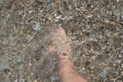 Tanned leg of a woman on a pebble beach against the sea and waves.