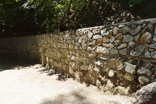 High stone fence along the pedestrian rural path in summer Sunny day.