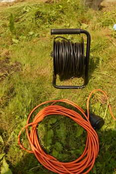 Coil with electric cable and extension cord on the grass, electric tools for construction works in the garden.