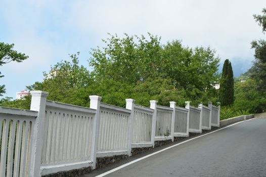 A paved road runs along the stone wall and cypress trees.