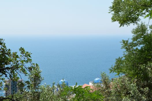 View of the sea coast and the beautiful roofs of the hotels through the framed trees.