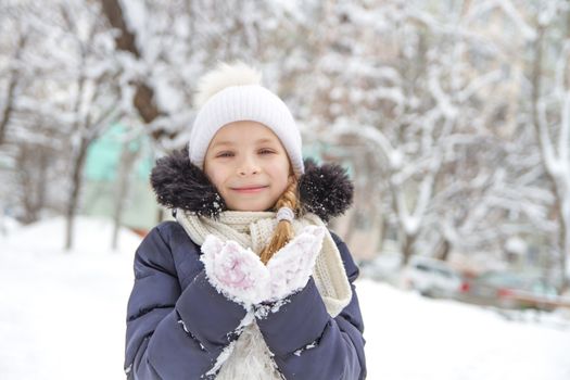 Smiling child girl playing with snow in winter park