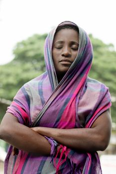 young veiled woman standing  outside and eyes closed praying .