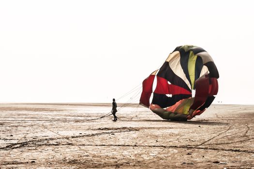 Man do some fold parachute after landing in a famous at Candolim Goa near Baga Beach and Vagator Beach. Yellow and blue wings slings are visible. Paragliding parachuting is extreme sport of recreation