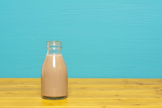 Chocolate milkshake in a one-third pint glass milk bottle, on a wooden table against a bright teal painted background