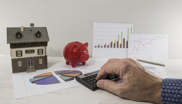 The hands of a man pushing the calculator, as a business and financial investment with a model of a house or planning of the construction of a house