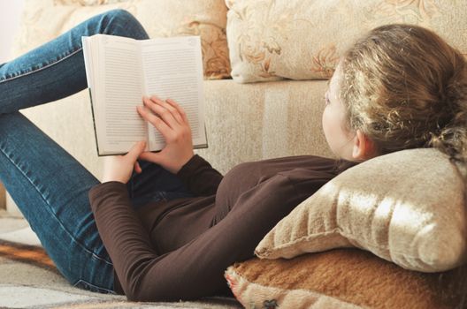 Young beautiful girl reading a book on the couch