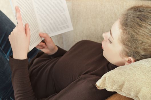 Young attractive girl reading a book on sofa