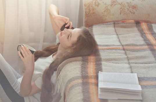 Happy Teen Girl Resting on Sofa at the Living Room While Reading her Favorite Novel Book and have a coffe