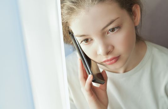 Portrait of a beautiful girl who speaks by telephone at home near windows, clouse-up