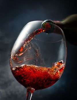 Wine pouring from bottle into wineglass on smoky background