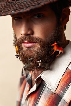 Young man in a cowboy hat and toy horses in a beard