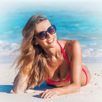 Young woman in bikini and sunglasses laying by tropical sea