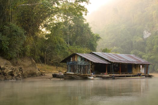 Amazing scenic view of the old house on the river among the rainforest with a jungle river on the background of green trees in the morning sun.