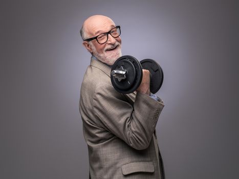 Happy funny senior man in suit with dumbbell, power concept