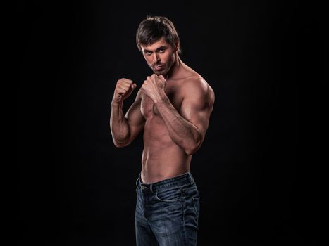 Muscular man in fighting stance holding fists ready to fight black background